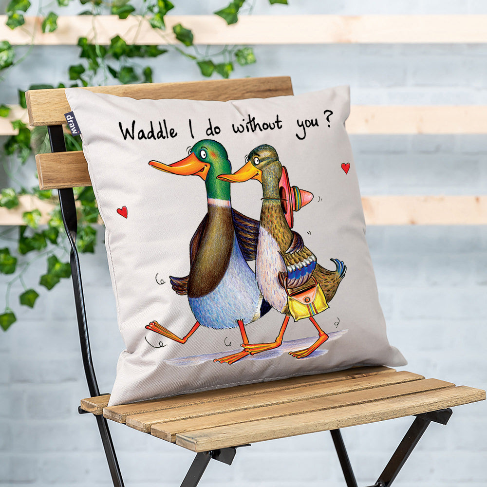 Cushion with two ducks and 'Waddle I do" slogan, on garden chair with white brick wall and green leaves in background