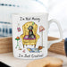A white ceramic coffee mug with a humorous illustration of a grey dog sitting in a yellow armchair, surrounded by scattered toys and the text 'I'm Not Messy.
